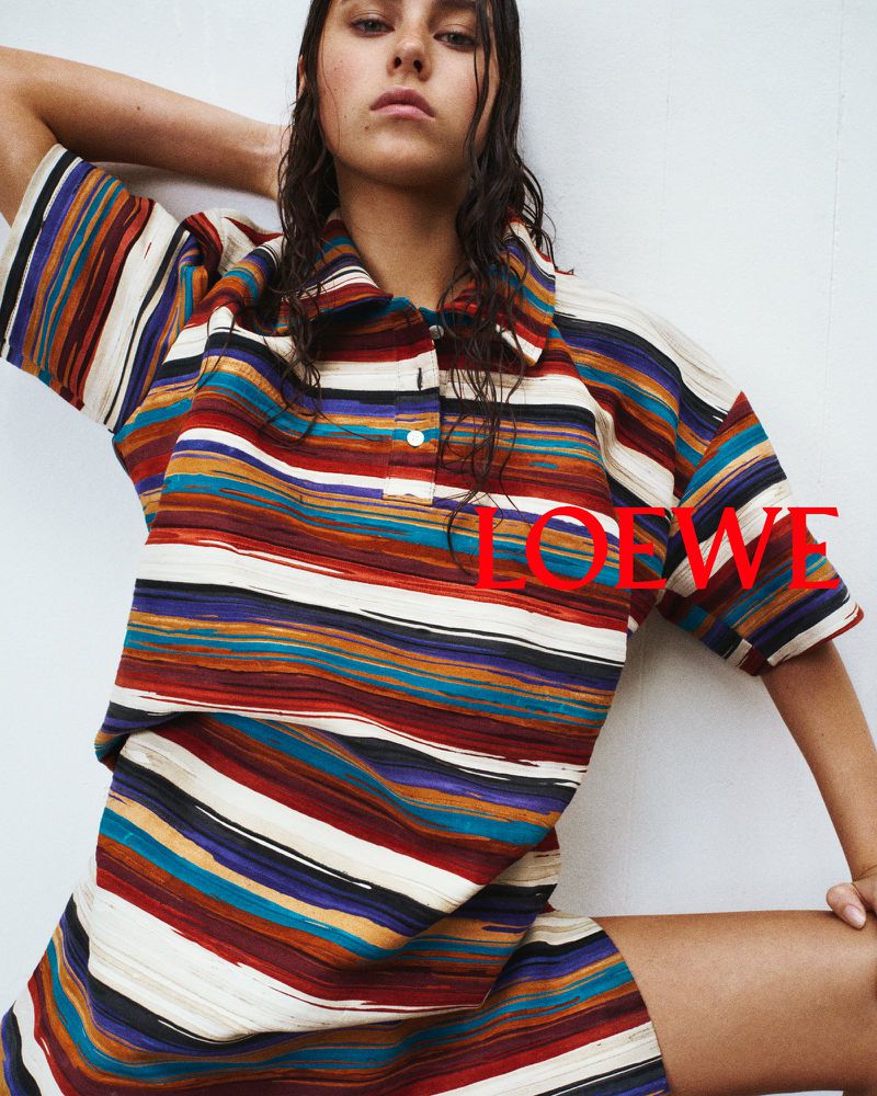 Woman with wet hair wearing a multi-coloured striped polo shirt and matching shorts against a white background