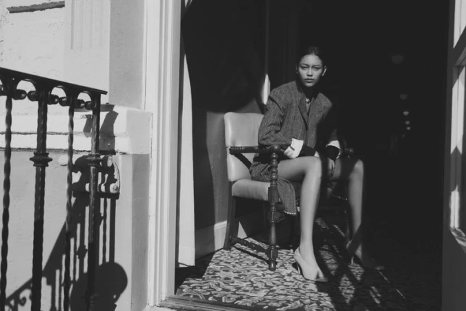 Monochrome fashion editorial portrait of a model seated in an armchair by a balcony for Vogue Polska.