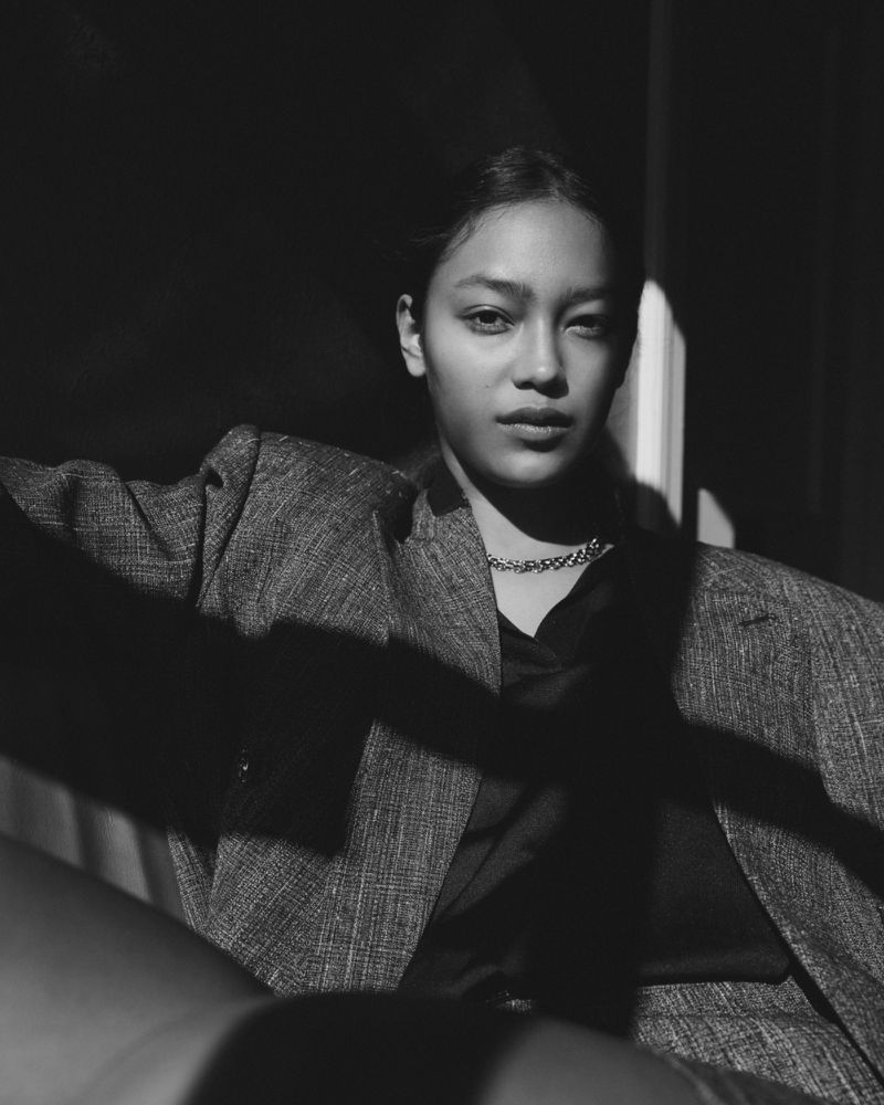 Monochrome portrait of a model in a tweed blazer and chain necklace under dramatic chiaroscuro lighting.