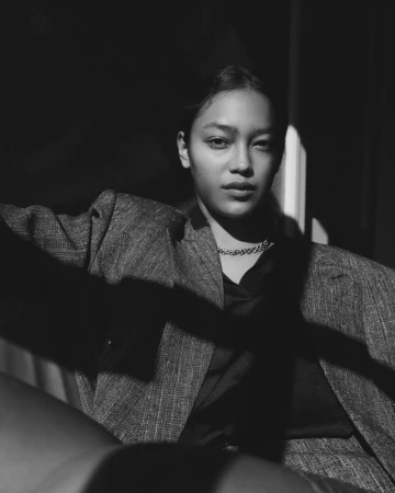 Monochrome portrait of a model in a tweed blazer and chain necklace under dramatic chiaroscuro lighting.