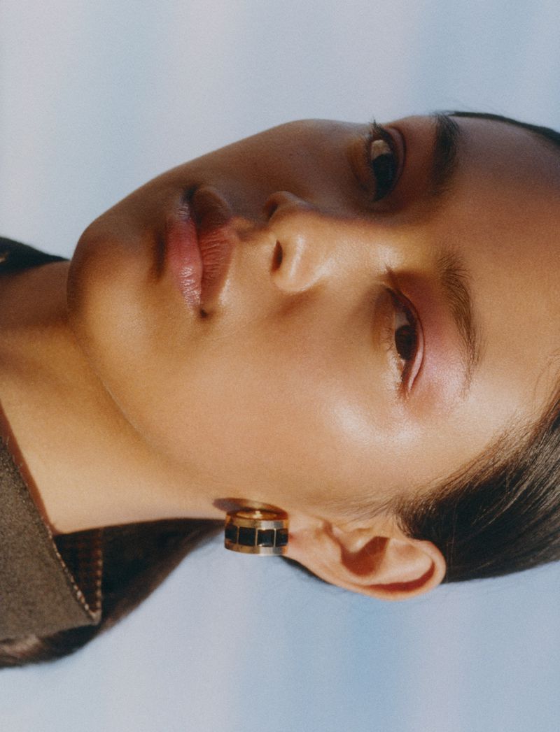Close-up beauty shot of an Asian adult female model in a fashion studio wearing large modern gold and black earrings. Soft lighting.