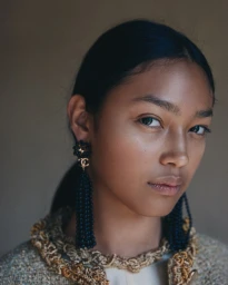 Close-up portrait of a model wearing ornate black beaded drop earrings and a textured tweed jacket for Vogue Polska.