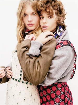 Two female models embracing against a white background, wearing patterned winter apparel and scarves.
