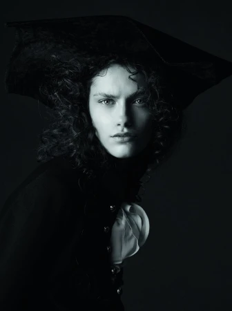 Dramatic black and white portrait of a person wearing a tricorn hat and ruffled shirt against a dark background in a photo studio.