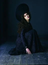 Model Julia Kuźniar kneeling in a dark tweed coat and large round hat for Telva magazine