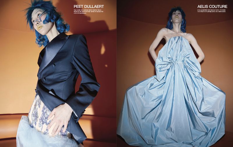 Two women in a studio, one in a black jacket and sequined skirt, the other in a light blue strapless gown, against an orange wall.