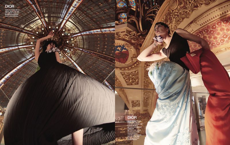 Fashion editorial shot from low angle featuring two women in ornate dresses in an opulent setting with detailed architectural features.