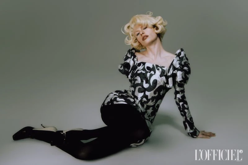 Elegant adult female fashion model poses in a silver and black patterned dress and black tights on a grey studio background. 