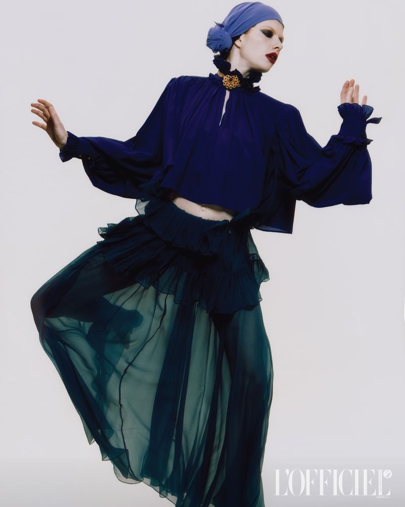 Model in dark blue blouse and sheer green skirt wearing a blue headscarf posing against a plain background for L'Officiel Hong Kong.