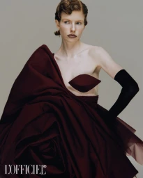 Model in voluminous burgundy dress with a long black glove against a grey studio background