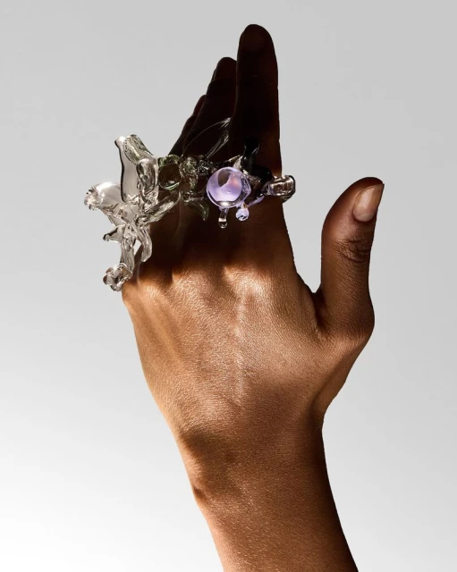 Close-up of a translucent decorative glass ring on the finger of a hand with a neutral gray background in a studio shot.