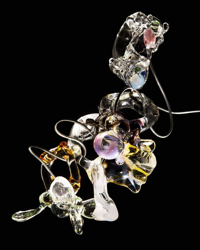 Abstract sculpture of transparent blown glass in clear, amber, and purple tones isolated on black background in studio lighting.