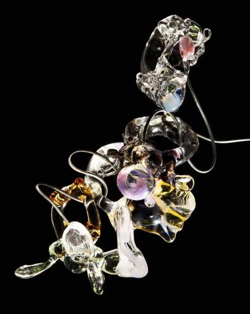 Abstract sculpture of transparent blown glass in clear, amber, and purple tones isolated on black background in studio lighting.