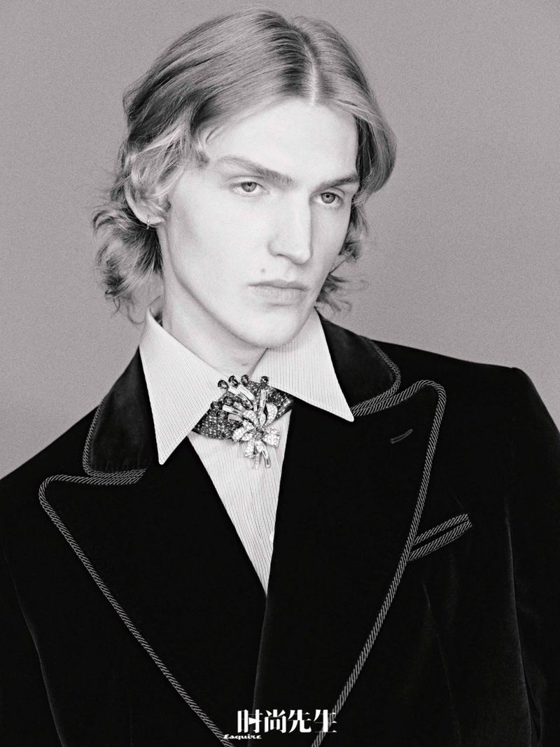 Portrait of a young adult male in a black velvet blazer with jeweled brooch, captured in black and white with soft, diffused lighting.