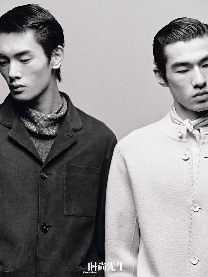 Monochrome studio shot of two Asian male fashion models in jackets and turtlenecks, showcasing modern menswear style with minimalist backdrop.