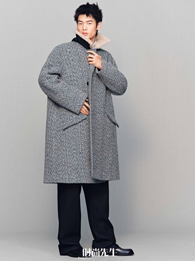 Portrait of a young adult man in a grey tweed overcoat with black trousers and dress shoes in a fashion editorial shot.
