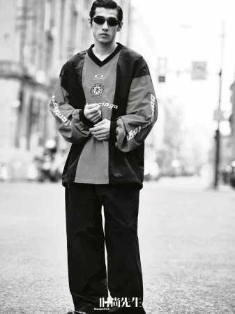 Monochrome portrait of Asian adult male in a sport-inspired fashion jacket and sunglasses, posing on a city street.