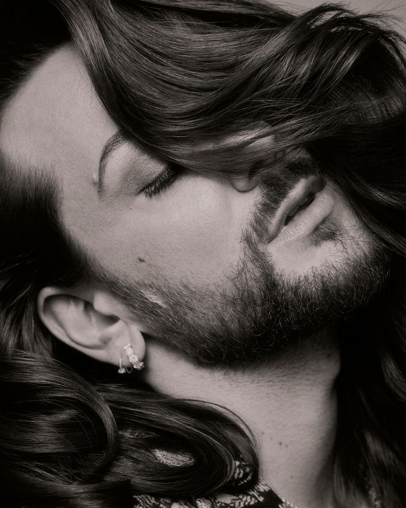 Close-up monochrome portrait of Riccardo Simonetti with flowing dark hair partially covering his face for Vogue Germany.