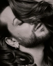 Close-up monochrome portrait of Riccardo Simonetti with flowing dark hair partially covering his face for Vogue Germany.