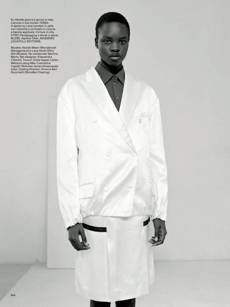 An African woman poses in a double-breasted, white satin jacket and skirt. A grey button-down shirt is worn underneath the jacket.