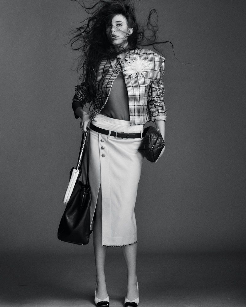 Monochrome fashion shot of a woman with windblown hair wearing a plaid jacket, skirt with a slit, and black-and-white heels.