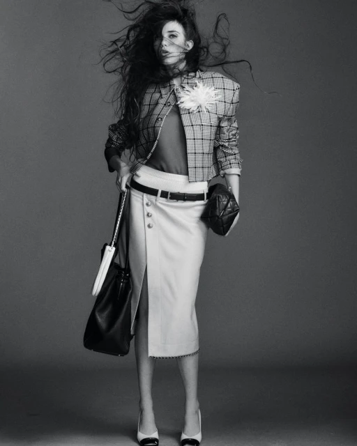 Monochrome fashion shot of a woman with windblown hair wearing a plaid jacket, skirt with a slit, and black-and-white heels.