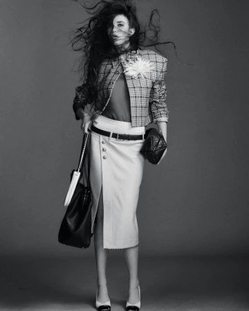 Monochrome fashion shot of a woman with windblown hair wearing a plaid jacket, skirt with a slit, and black-and-white heels.