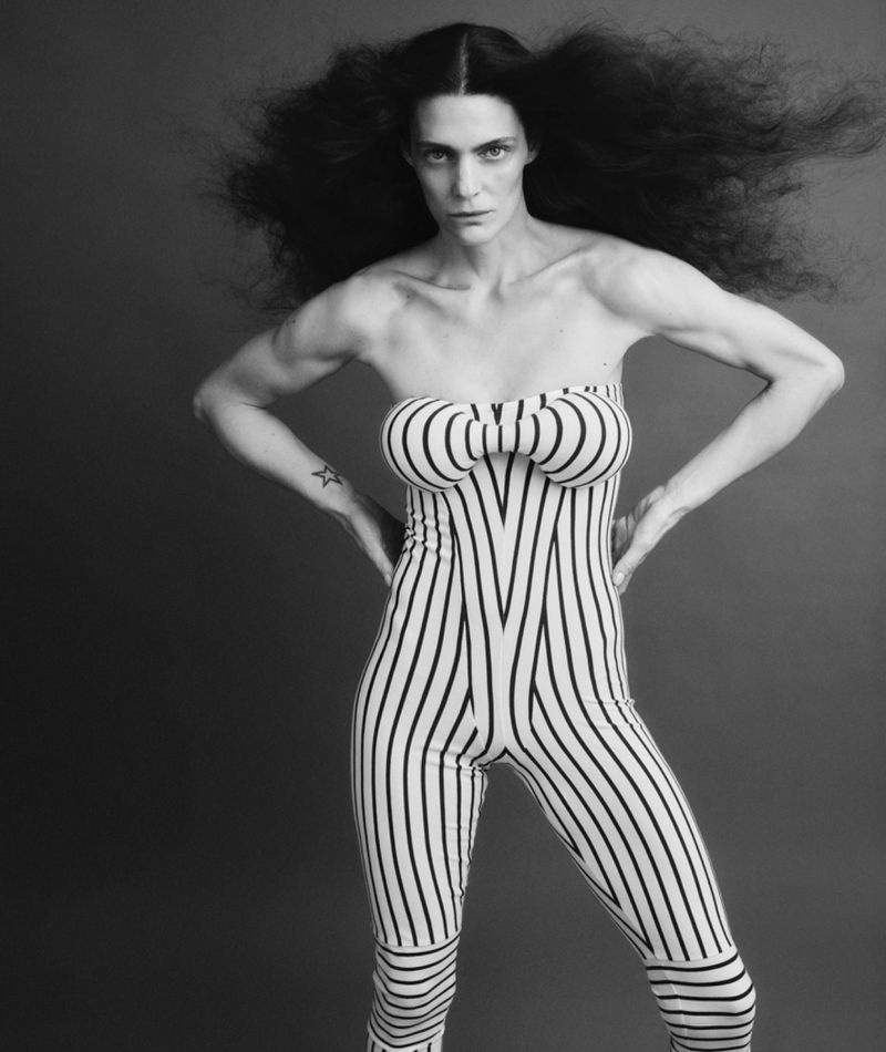 Monochrome portrait of a slender adult female model with voluminous dark hair wearing a black and white striped strapless jumpsuit.