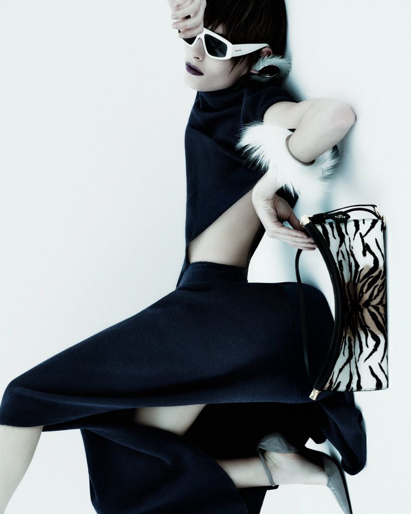 Fashionable adult female strikes a pose in a cutout dress with stylish glasses and a zebra-print handbag, set against a clean white backdrop.