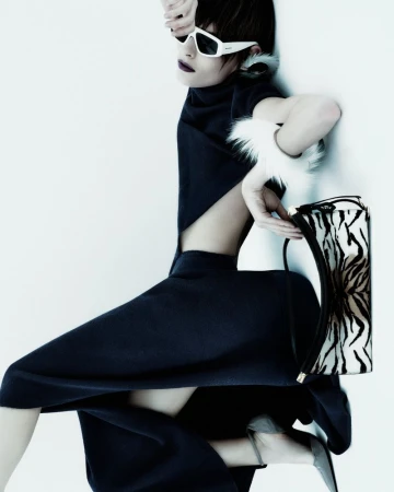 Fashionable adult female strikes a pose in a cutout dress with stylish glasses and a zebra-print handbag, set against a clean white backdrop.