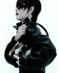 Profile portrait of a short-haired model wearing a black leather jacket and pearl earrings, holding handbags against a white background.