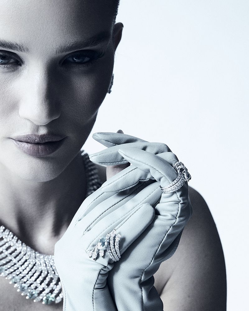 Close-up of a woman posing with jewelry: diamond necklace, earrings, rings, and gloves against a light background in a fashion shot.