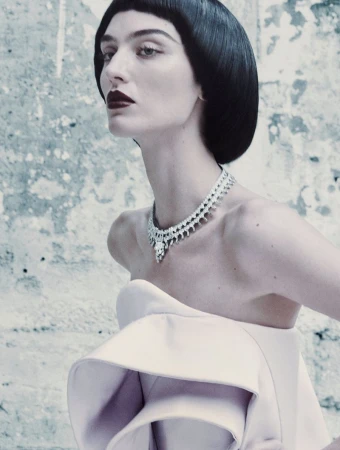 Model with dark bob hairstyle wearing a structured pale pink strapless top and diamond necklace against a weathered wall