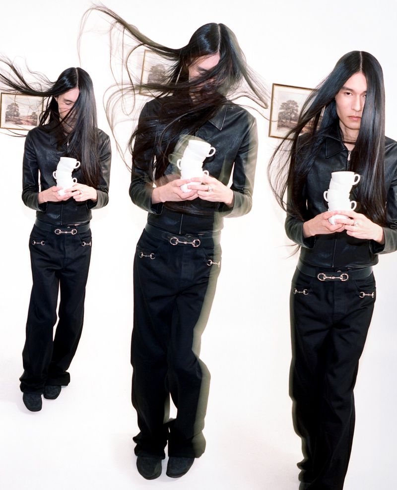 Model in a black leather jacket and pants holds a stack of white cups in a photo studio setting with multiple exposures.