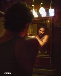 Actor Avan Jogia looking into a bathroom mirror in a moody dimly lit room for Paper Magazine.