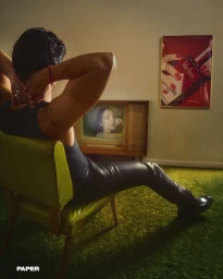 A man seated in a green armchair viewed from behind, watching a vintage television displaying a woman's face.