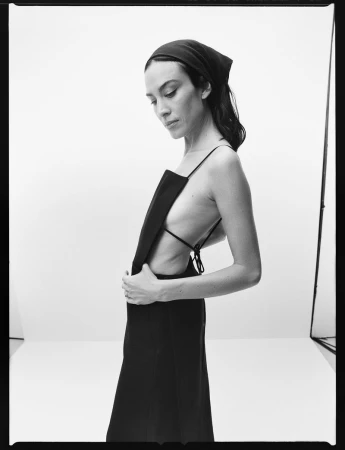 Monochrome studio portrait of a slender woman with dark hair and a headscarf, wearing a dark dress with a strappy back.