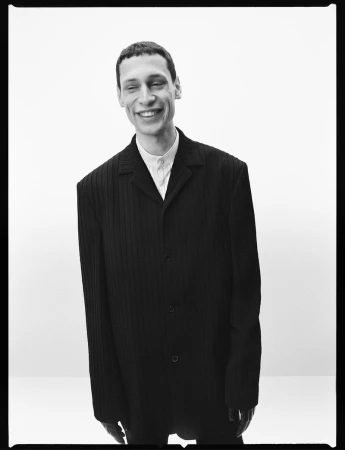 Monochrome portrait of a smiling man in a dark blazer against a white background for Calvin Klein Collection Fall 2026