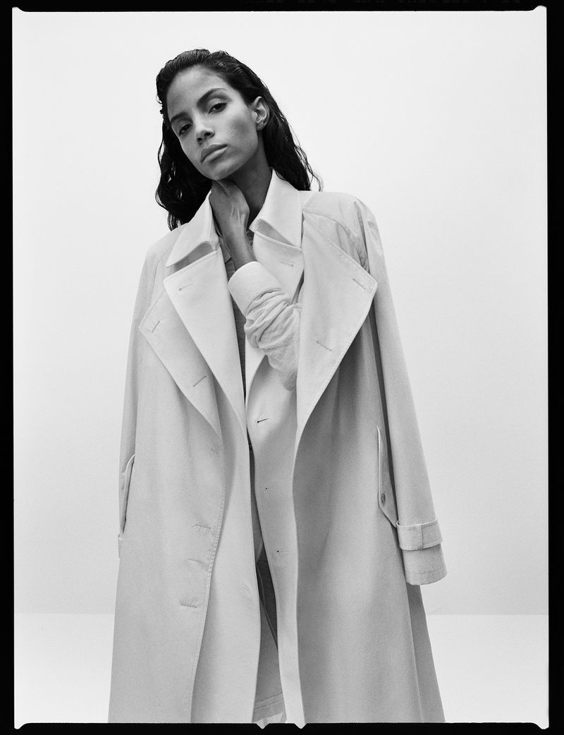 Monochrome portrait of a woman in a light-colored trench coat against a neutral backdrop, showcasing a fashion editorial aesthetic.