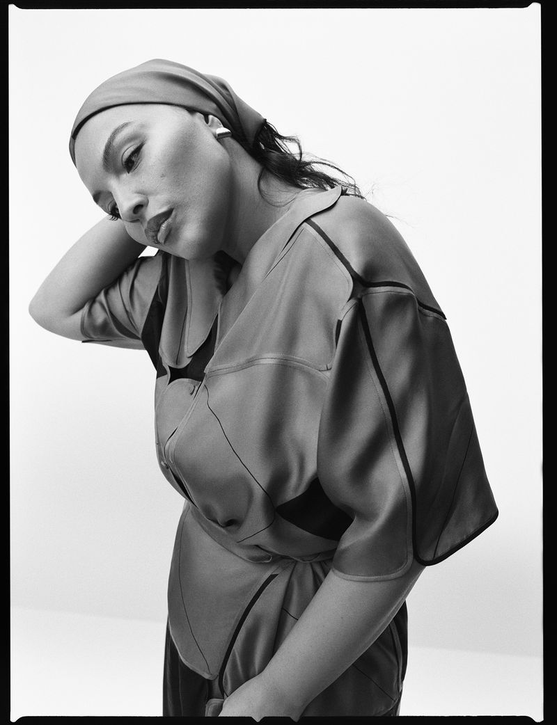 Monochrome portrait of a woman with a headscarf, posing with her head tilted to the side in a studio setting with soft lighting.