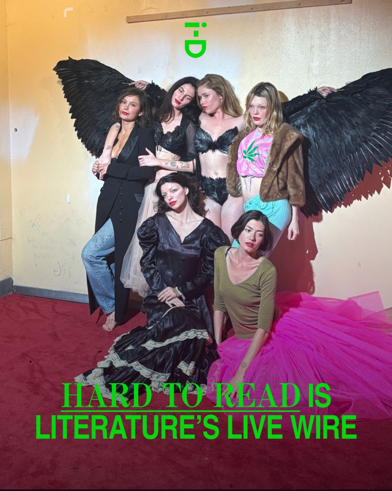 Six women pose together in a studio with wings attached to their backs, in a dimly lit room, with the 'i-D' logo visible on the wall.