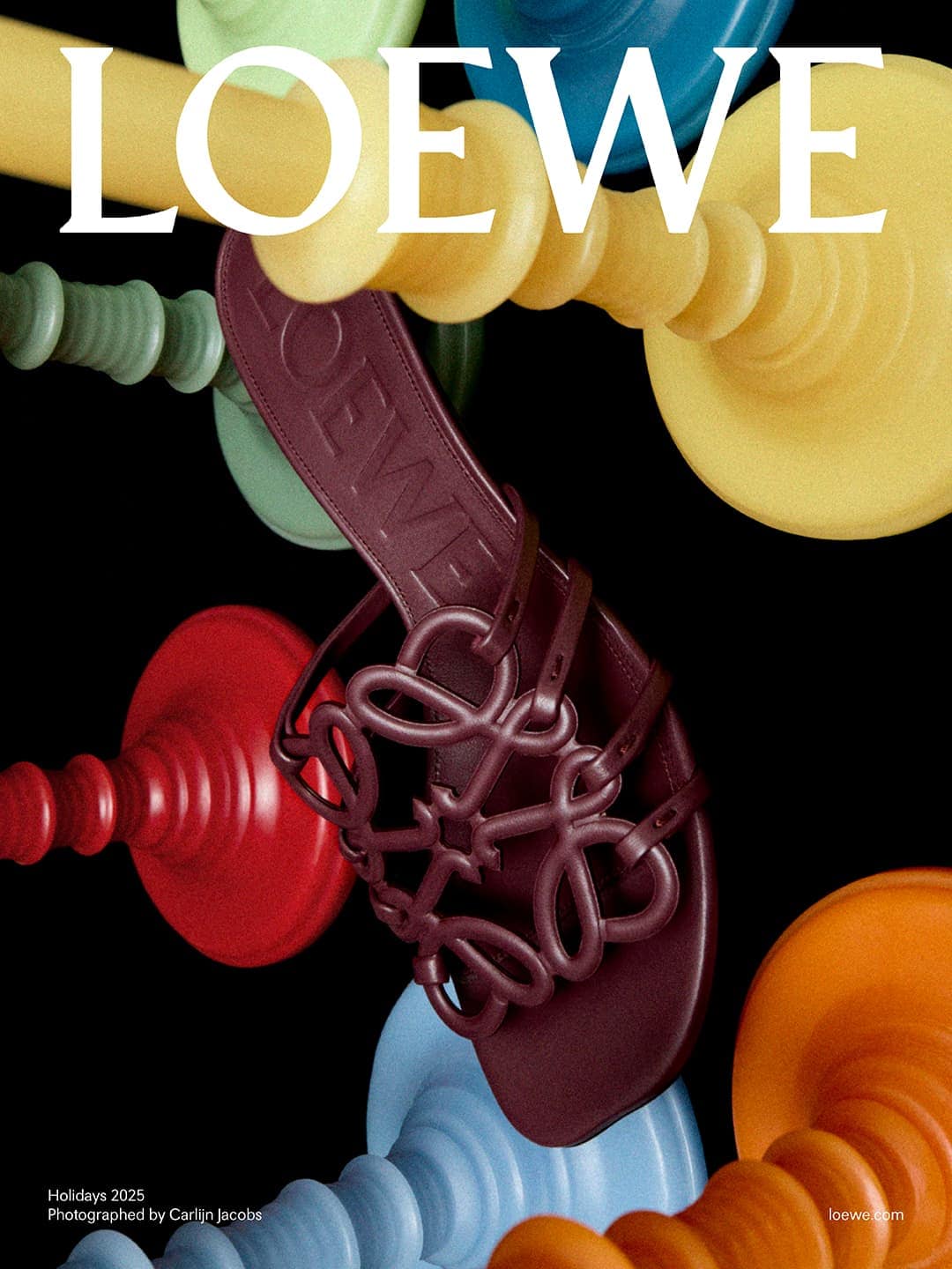 Loewe sandal still life: Brown leather sandal with Loewe logo, colorful wooden ornaments, and black background. Fashion-forward footwear.