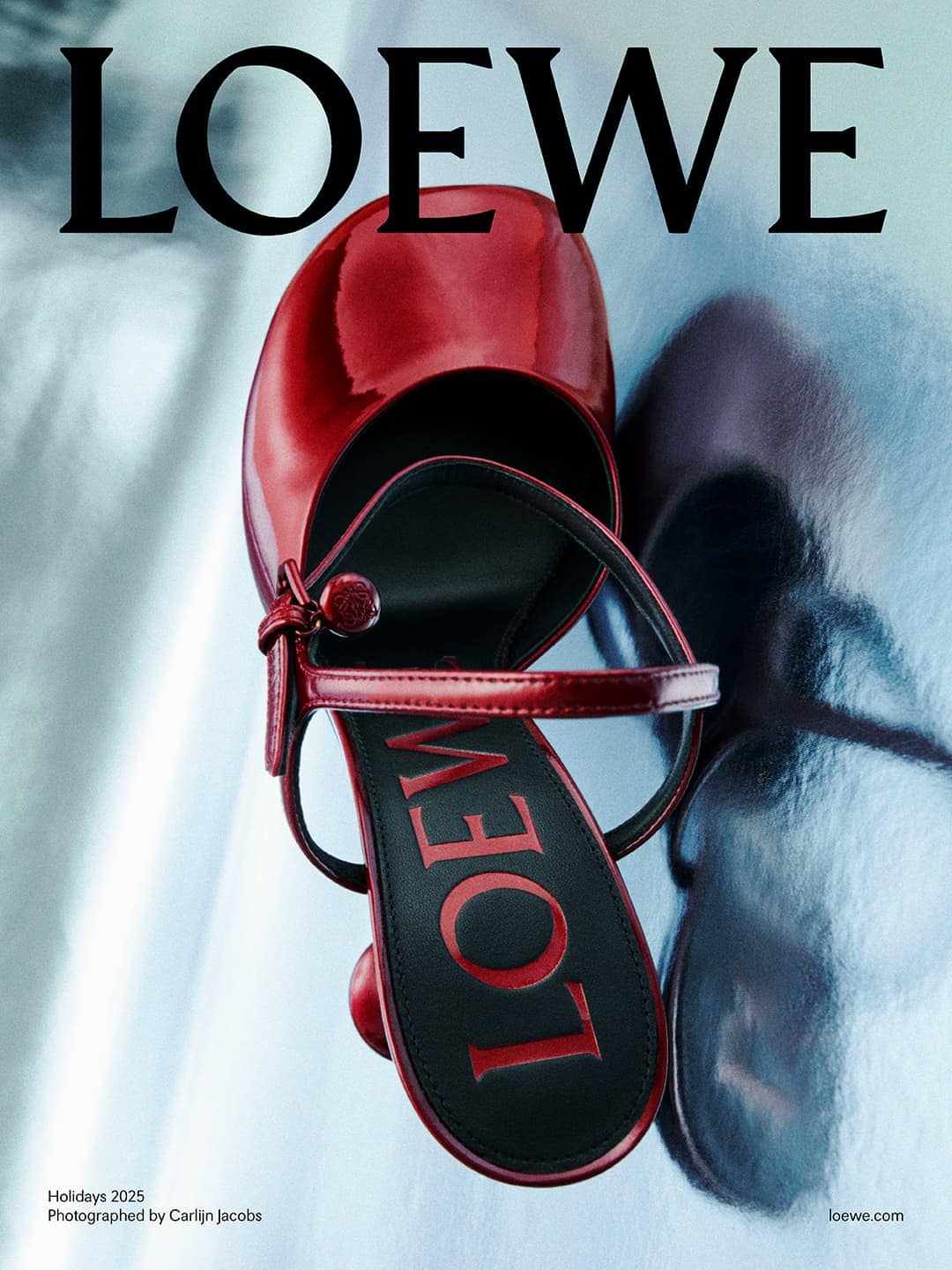 Close-up of a red patent leather heeled sandal by Loewe, displayed on a silvery, shimmering surface, advertising Loewe Holidays 2023.