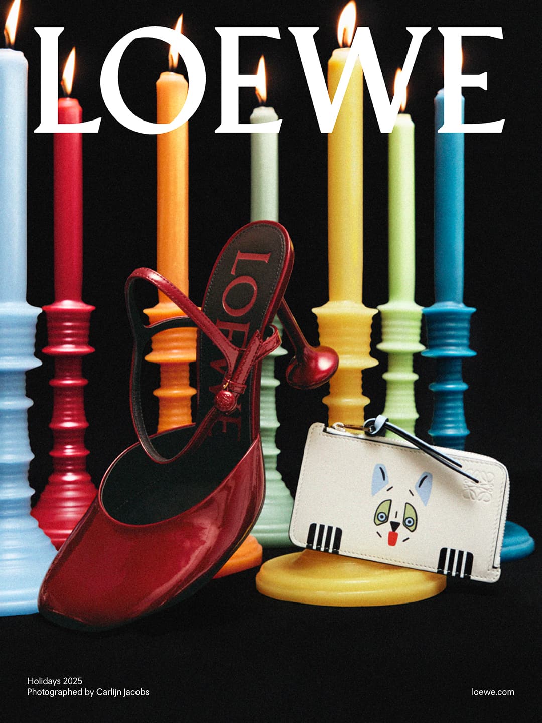 Still life shot of a red Mary Jane heel, a white card holder featuring an animal illustration, and colorful candles on a black surface.