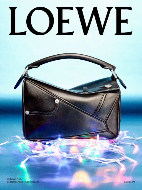 Loewe black leather Puzzle bag sits on a blue surface with festive string lights, showcasing a sleek design and holiday ambiance.