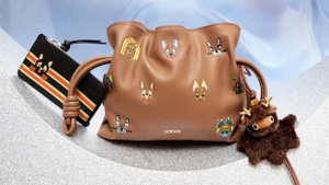 Brown leather handbag decorated with colourful animal patches, alongside a black wallet and fuzzy creature bag charm.