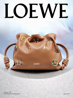 Tan leather Loewe handbag with knotted handles and decorative patches displayed on a curved gray textured surface.