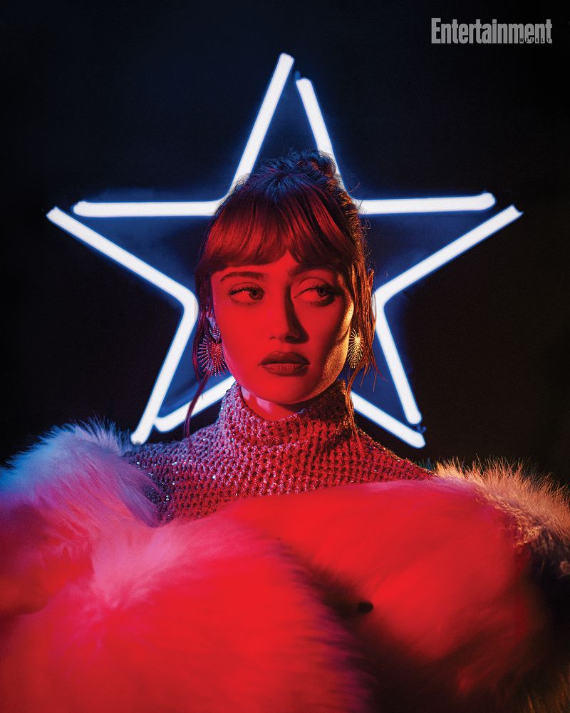Portrait of a woman with a sequined top and faux fur boa, illuminated by red light, with a star-shaped neon light behind her.