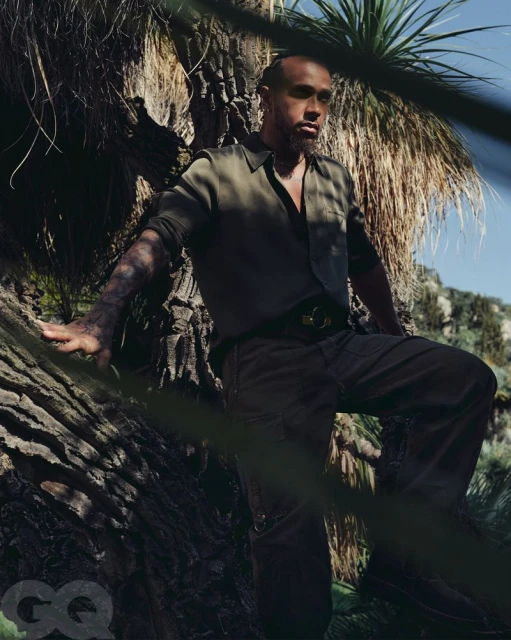 Portrait of adult male on tree with green shirt and dark pants outdoors in nature with arid plants in the background and magazine logo.