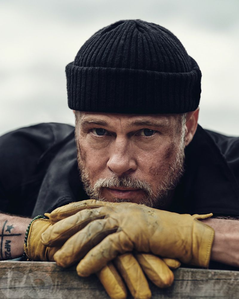 Portrait of adult male wearing a beanie and yellow gloves, resting chin on hands, close-up shot, neutral expression, studio lighting.